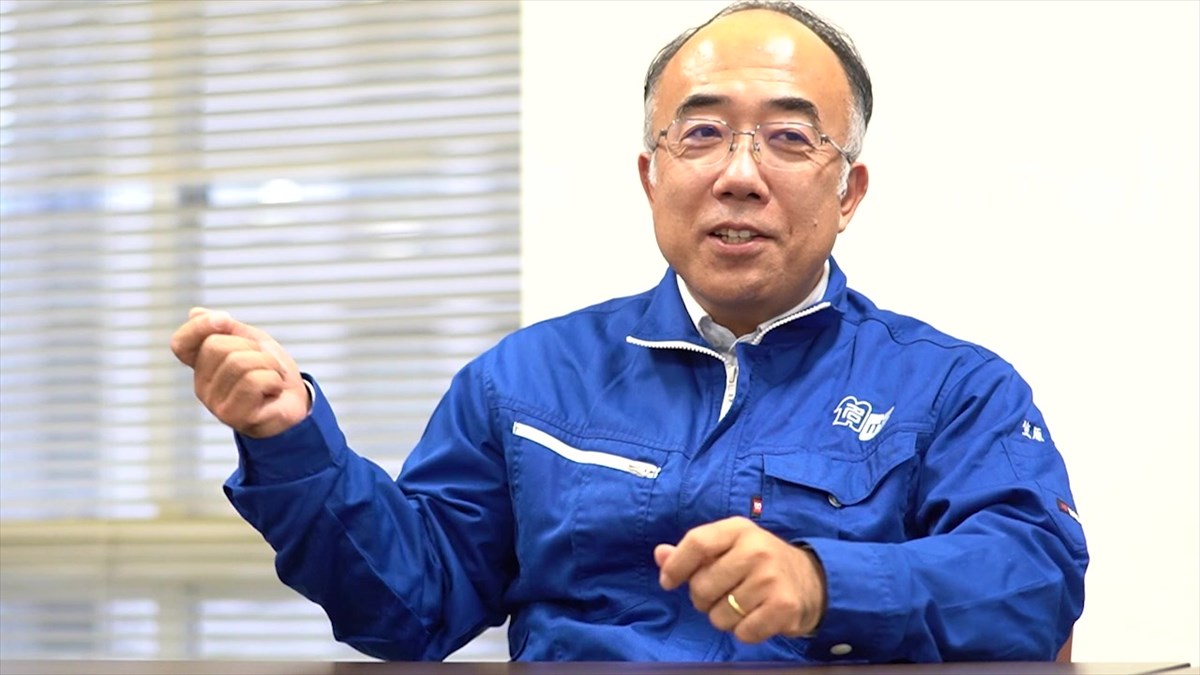 教授 笠原 次郎名古屋大学のマークの入った青い作業着を着用して話をしている。
